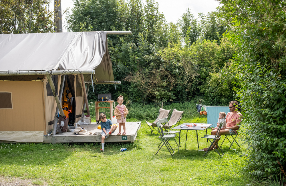 Famille avec deux enfants devant leur hébergement de camping au camping Huttopia Normandie
